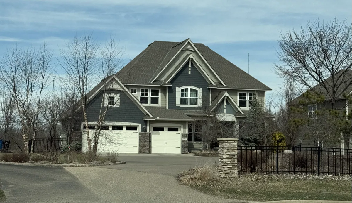 A blue-grey craftsman two-story home behind an iron fence on an Arden Hills street