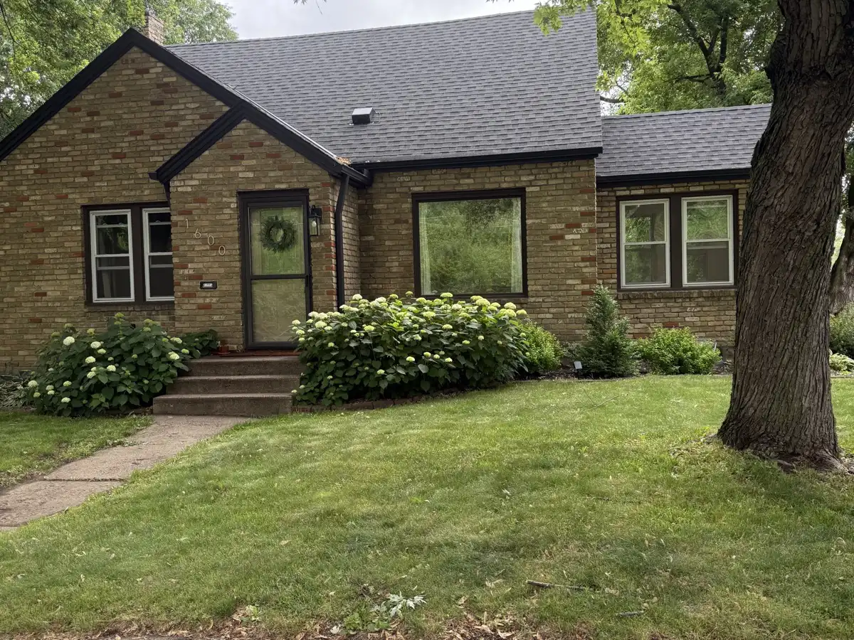 Established brick home shaded by a mature tree on a Blaine residential street in summer