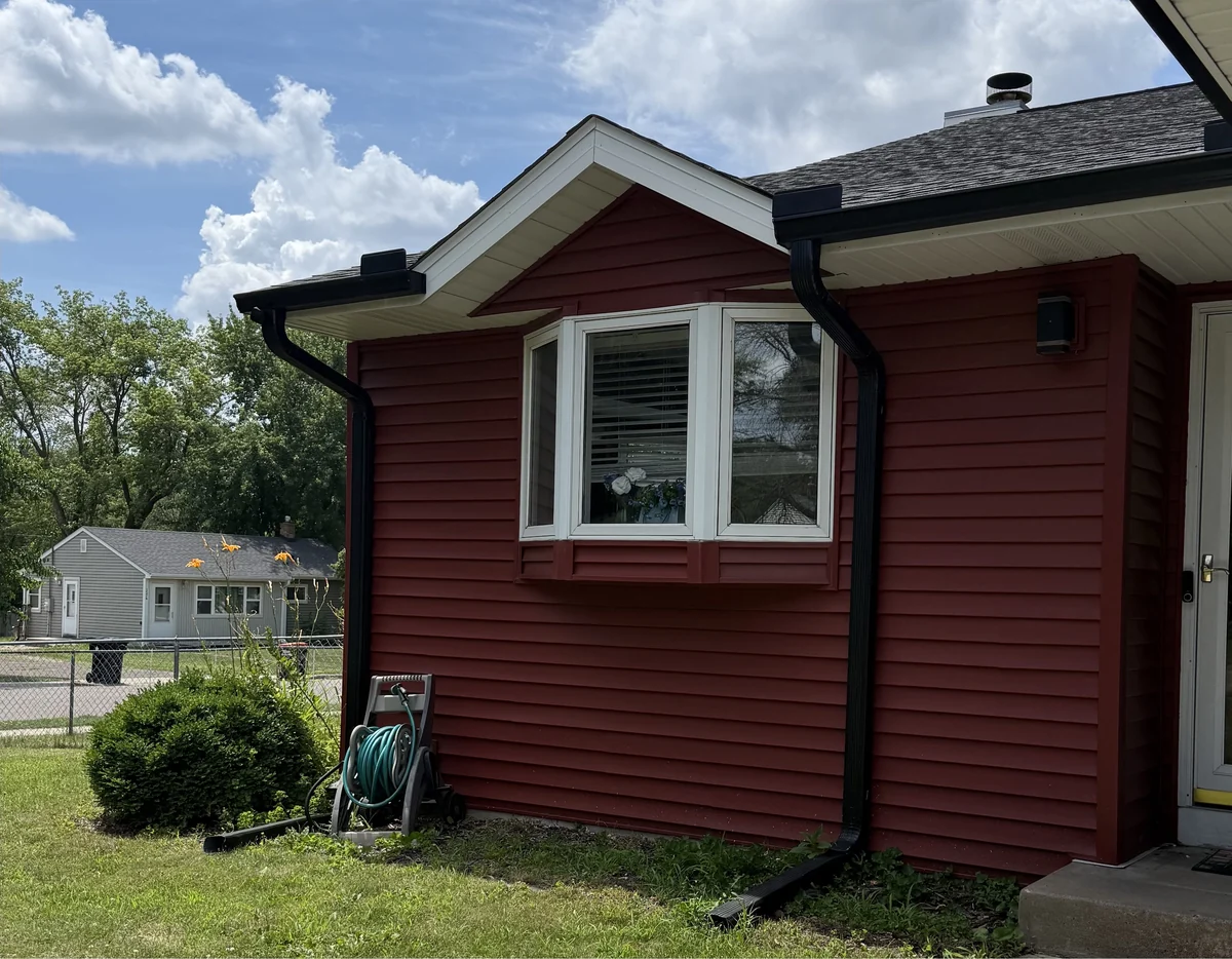 Red-sided rambler in Coon Rapids with a white bay window, mature shrubs and a fenced yard
