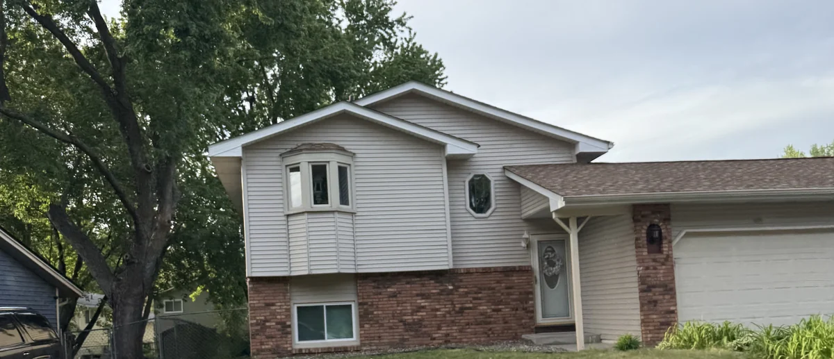 Split-level home in Coon Rapids with brick and siding, a bay window and a mature boulevard tree