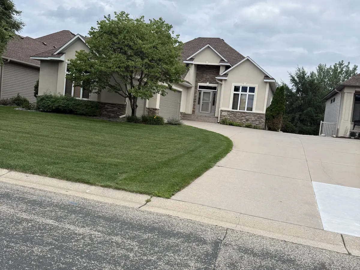 Two-story stucco and stone home with a mature front-yard tree in Deacon's Walk, Blaine